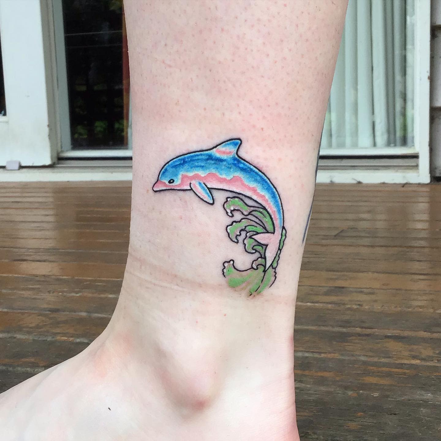 Tattoo of a dolphin jumping over green waves above an ankle