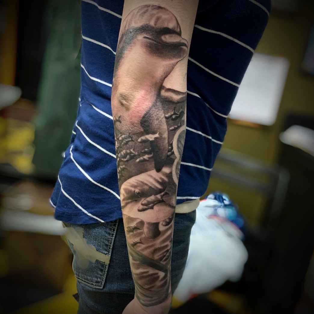 Full-arm tattoo featuring a realistic dolphin and aquatic scenery