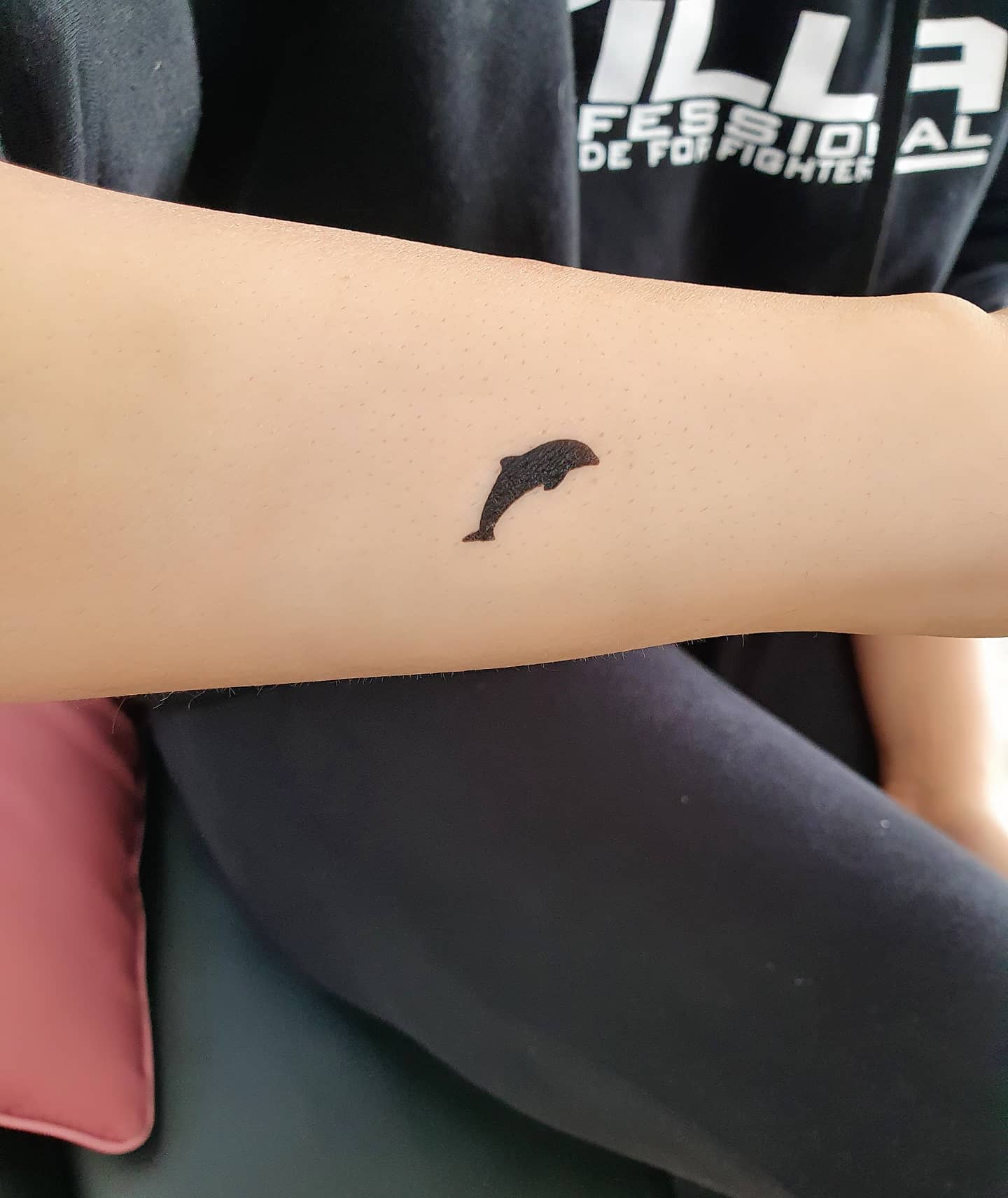 A small black dolphin tattoo on a forearm