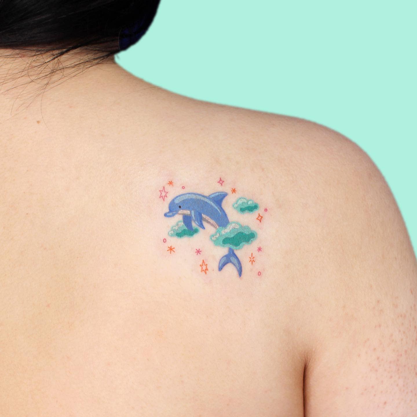 Colorful tattoo of a dolphin among clouds and stars on the upper back