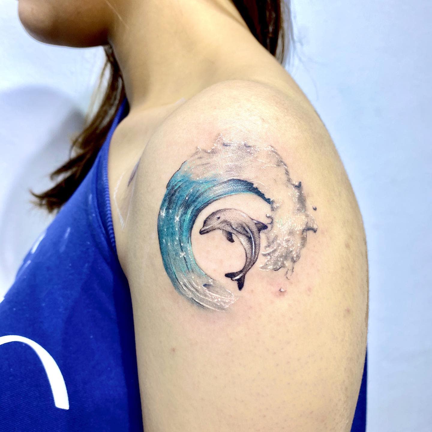 Tattoo of a dolphin leaping through a wave on an upper arm