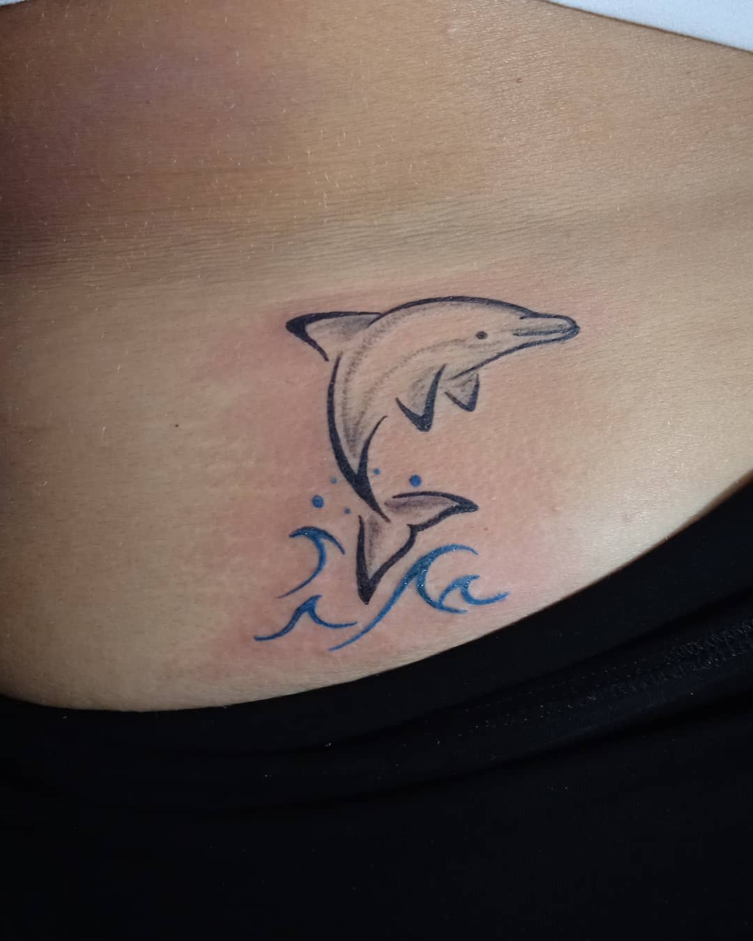 Tattoo of a dolphin jumping over blue waves on skin