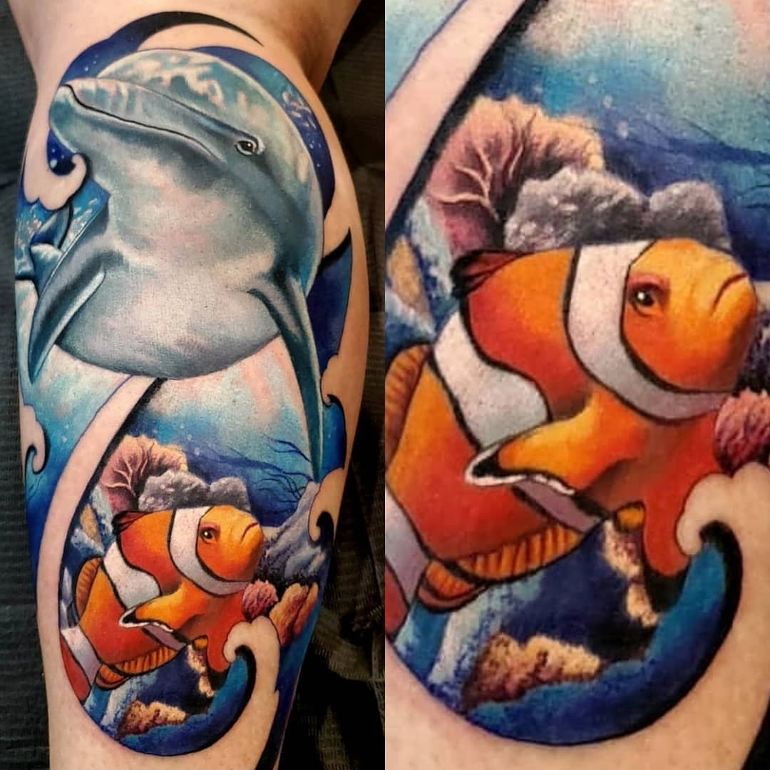 Tattoo featuring a shark, clownfish, and coral reef on an arm