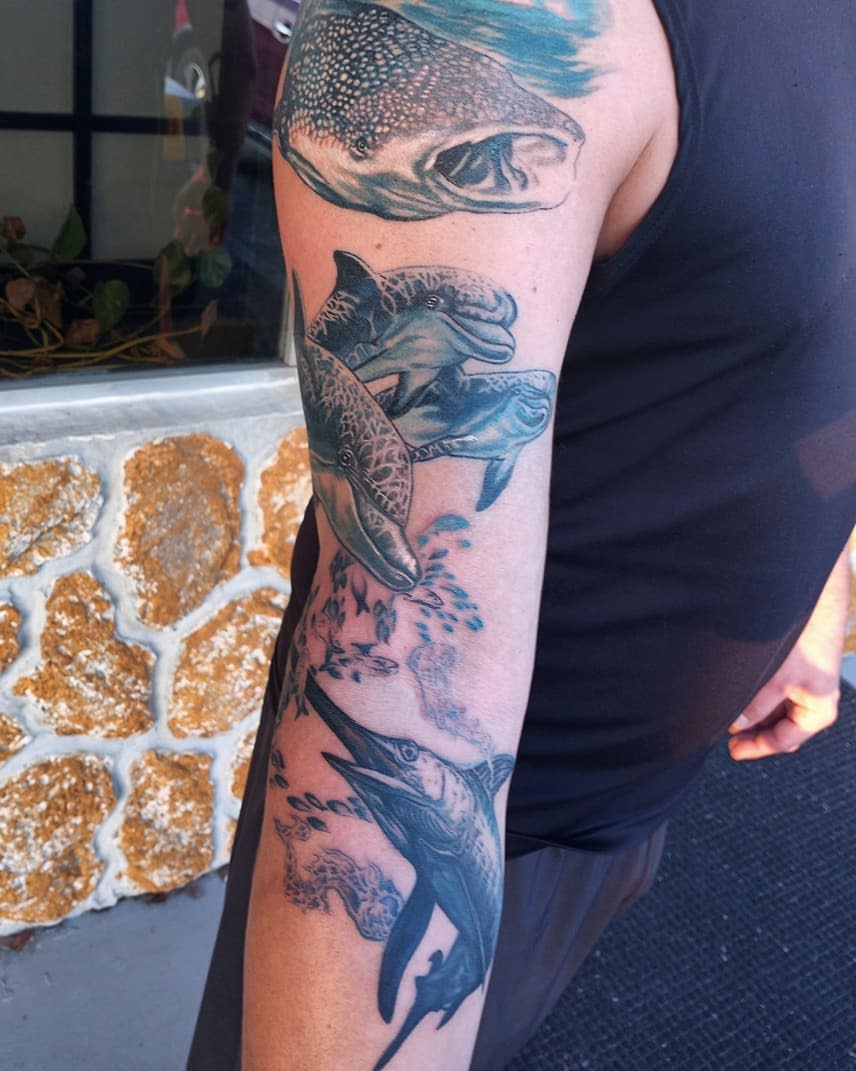 Arm tattoo featuring oceanic life with dolphins, sharks, and fishes
