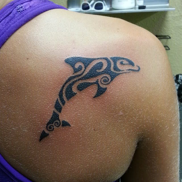 A tribal-style dolphin tattoo on the upper back