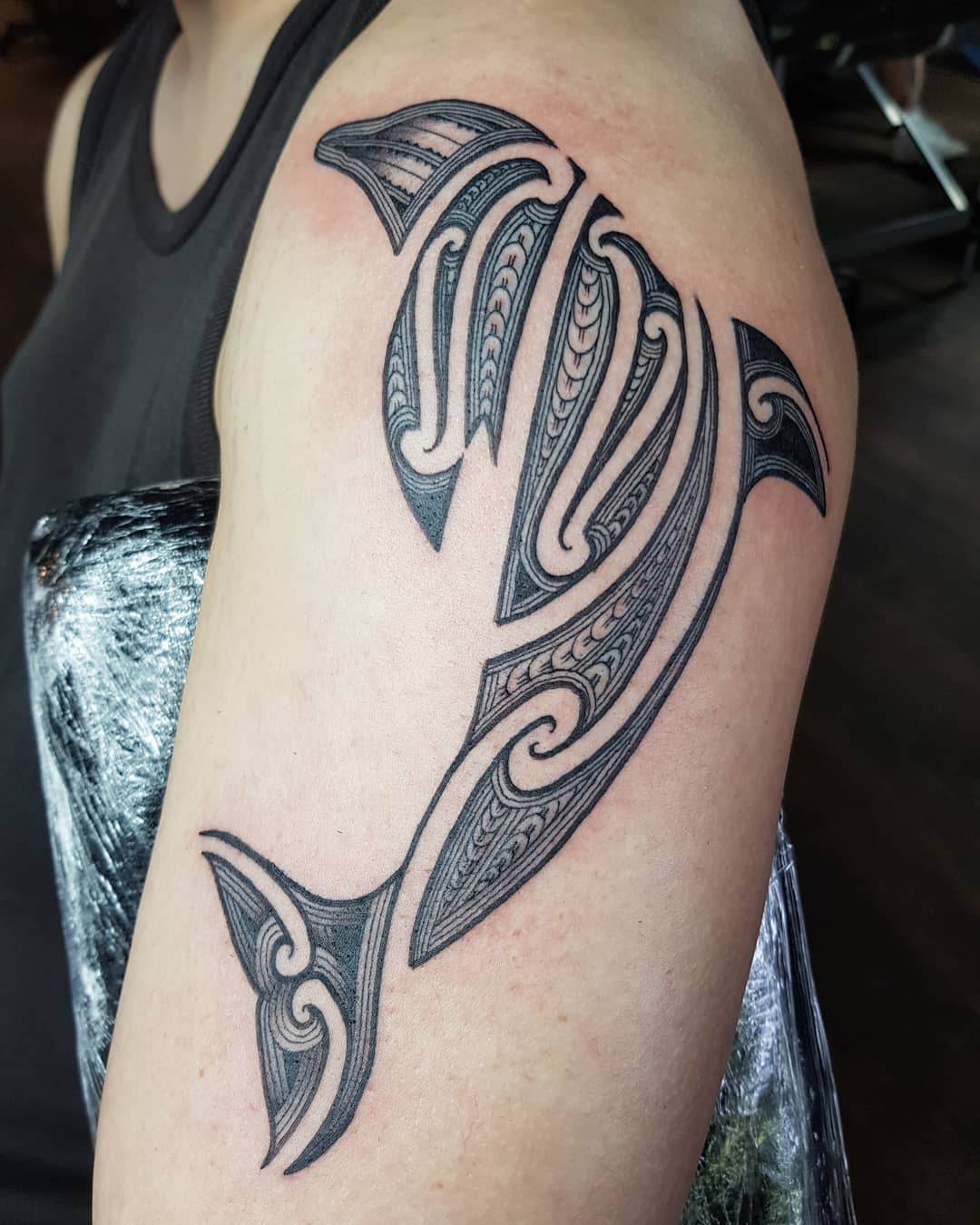 Upper arm tattoo of a stylized, tribal design dolphin