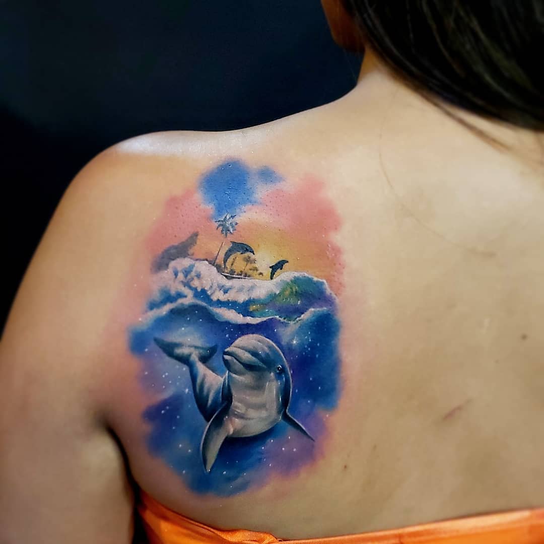 Colorful tattoo of dolphins and landscape on a woman's back