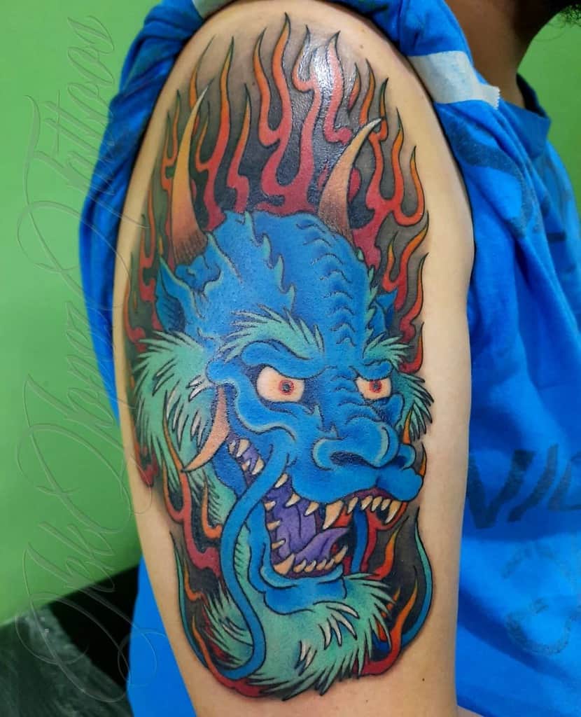 A vibrant tattoo of a dragon head with flames graces a person's upper arm