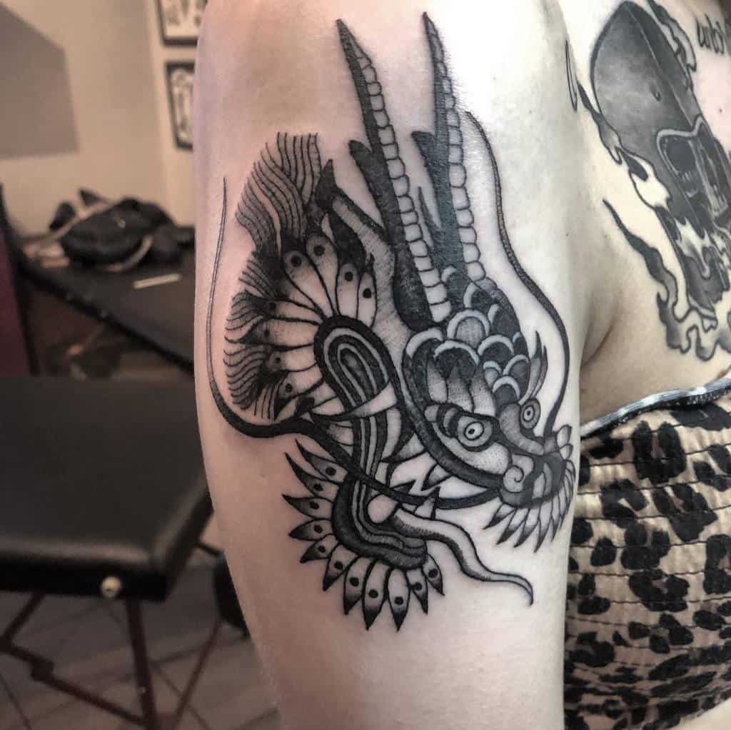 Intricately detailed black dragon tattoo with a striking head on the upper arm