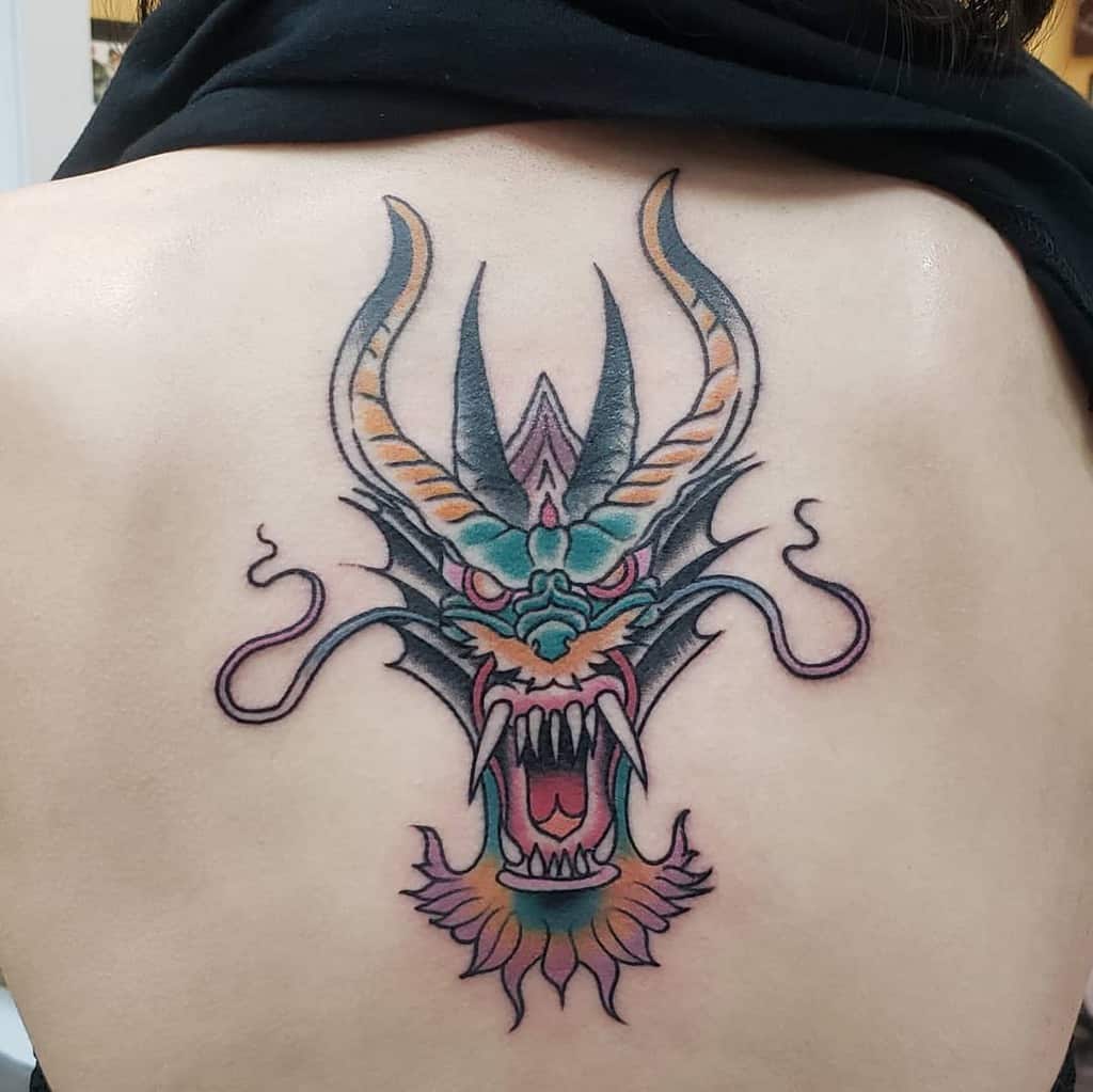 A fierce dragon tattoo, its head adorned with striking horns and an open mouth, sprawls majestically across a person's back