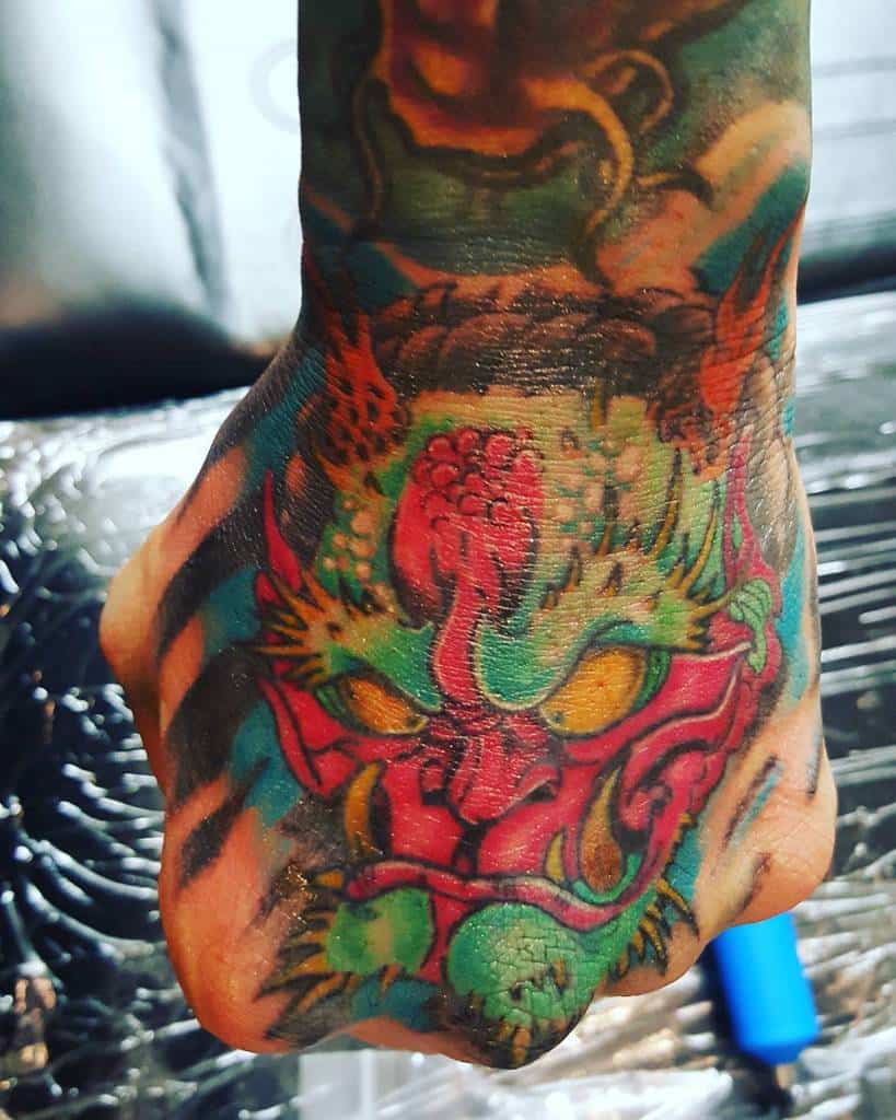 A colorful dragon tattoo on a hand, its head adorned with vibrant reds, greens, and yellows