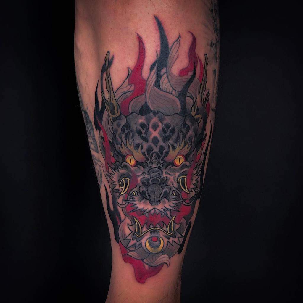 Tattoo of a fierce dragon head, intricately crafted in bold black and vibrant red hues, adorning a person's leg