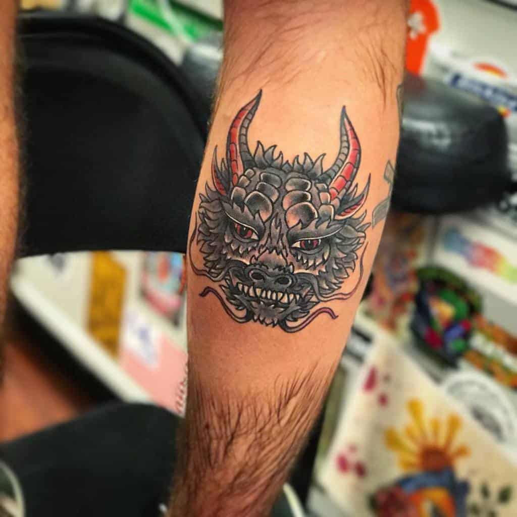 Tattoo of a fierce dragon head with horns on a person's inner forearm