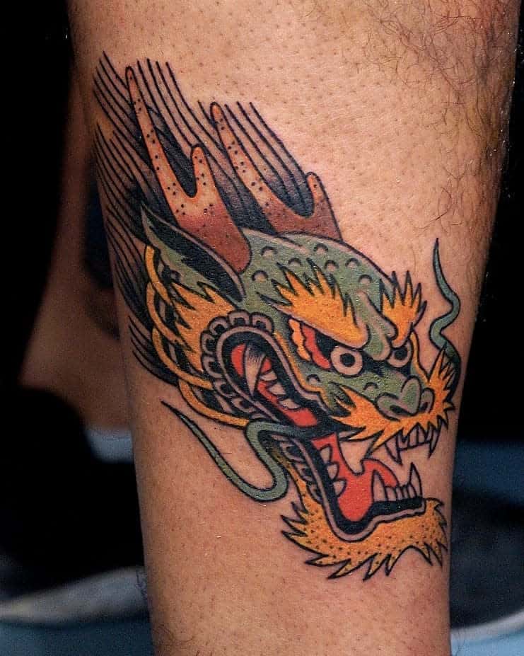 A vibrant tattoo featuring the majestic head of a colorful dragon adorns the person's leg, capturing attention with its intricate details