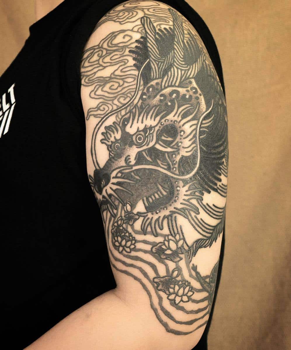 Close-up of an arm tattoo featuring a detailed dragon design with flowers and clouds