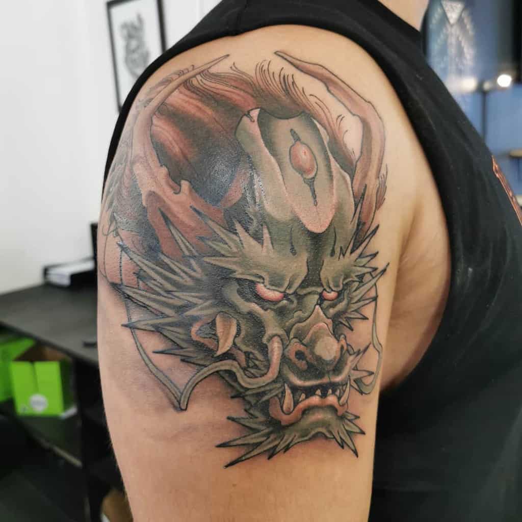 Colorful upper arm tattoo featuring a fierce dragon's face with intricate details, bold shading, and vibrant red and green tones