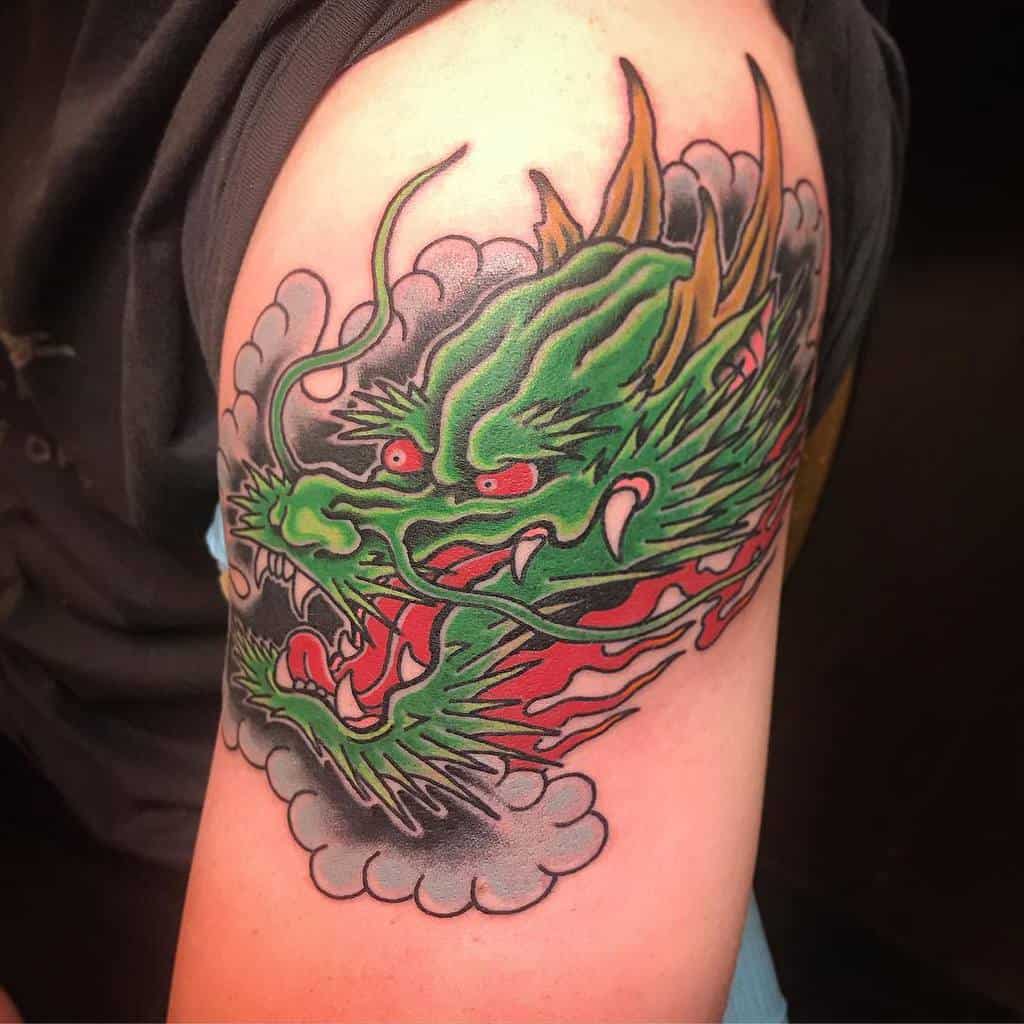 Bold upper arm tattoo of a green dragon with red accents, surrounded by clouds and intricate details in vibrant colors