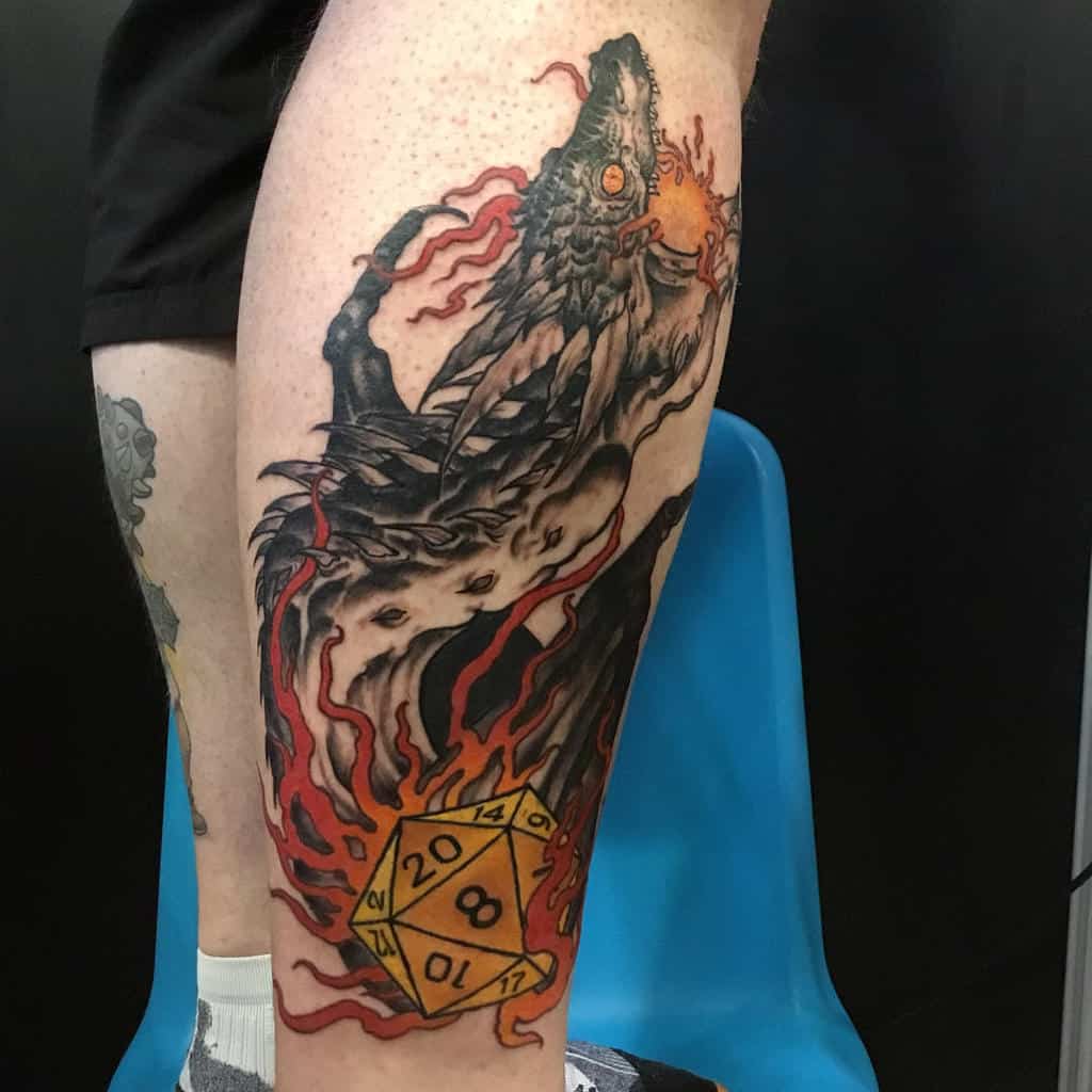 Detailed leg tattoo of a wolf-like dragon with fiery accents and a glowing D20 dice