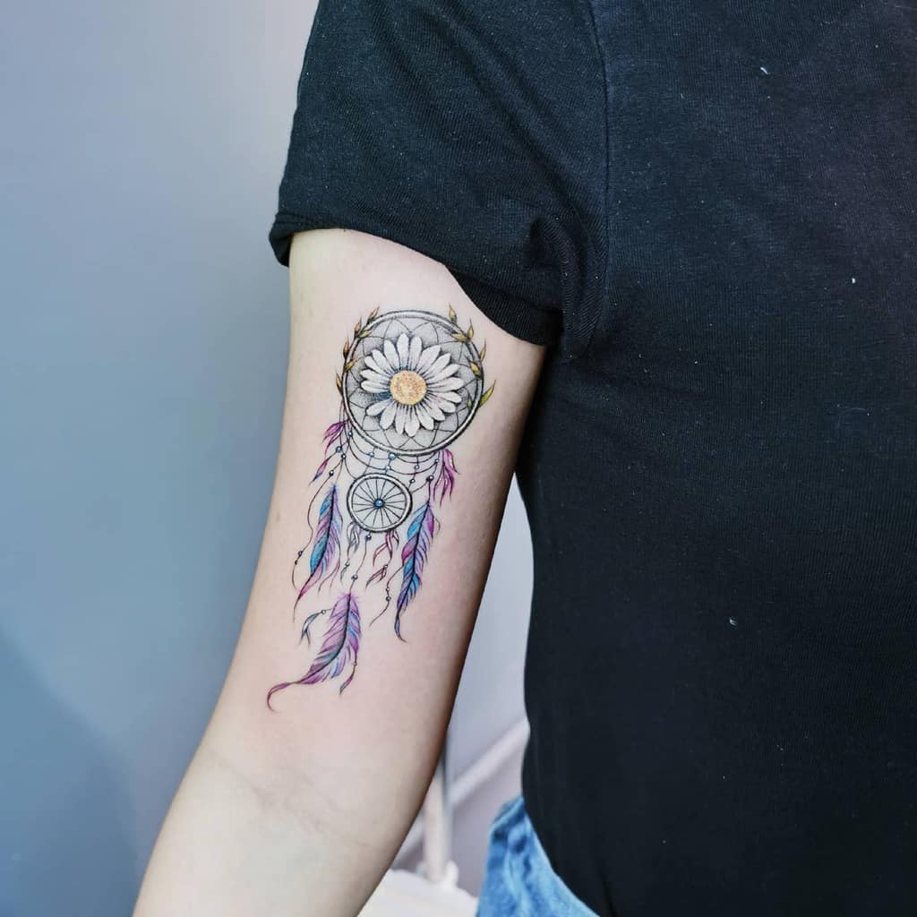 Dreamcatcher tattoo with flower and colorful feathers on an upper arm