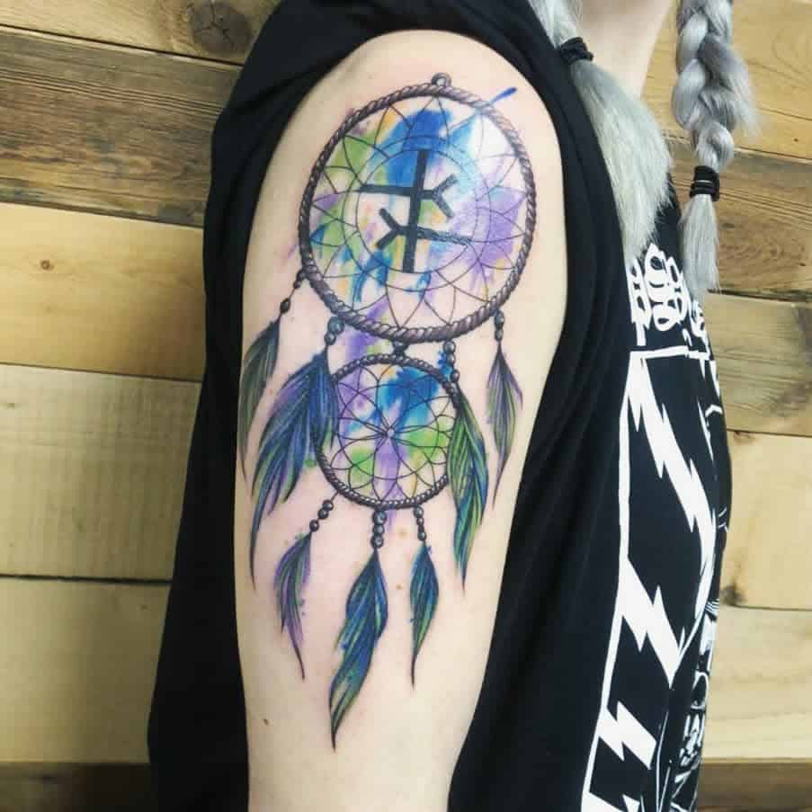 Colorful dreamcatcher tattoo with two circles and feathers on an upper arm