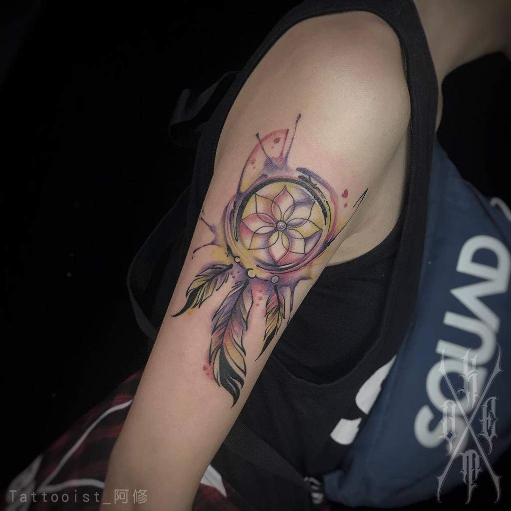 A colorful dreamcatcher tattoo with feathers on an upper arm