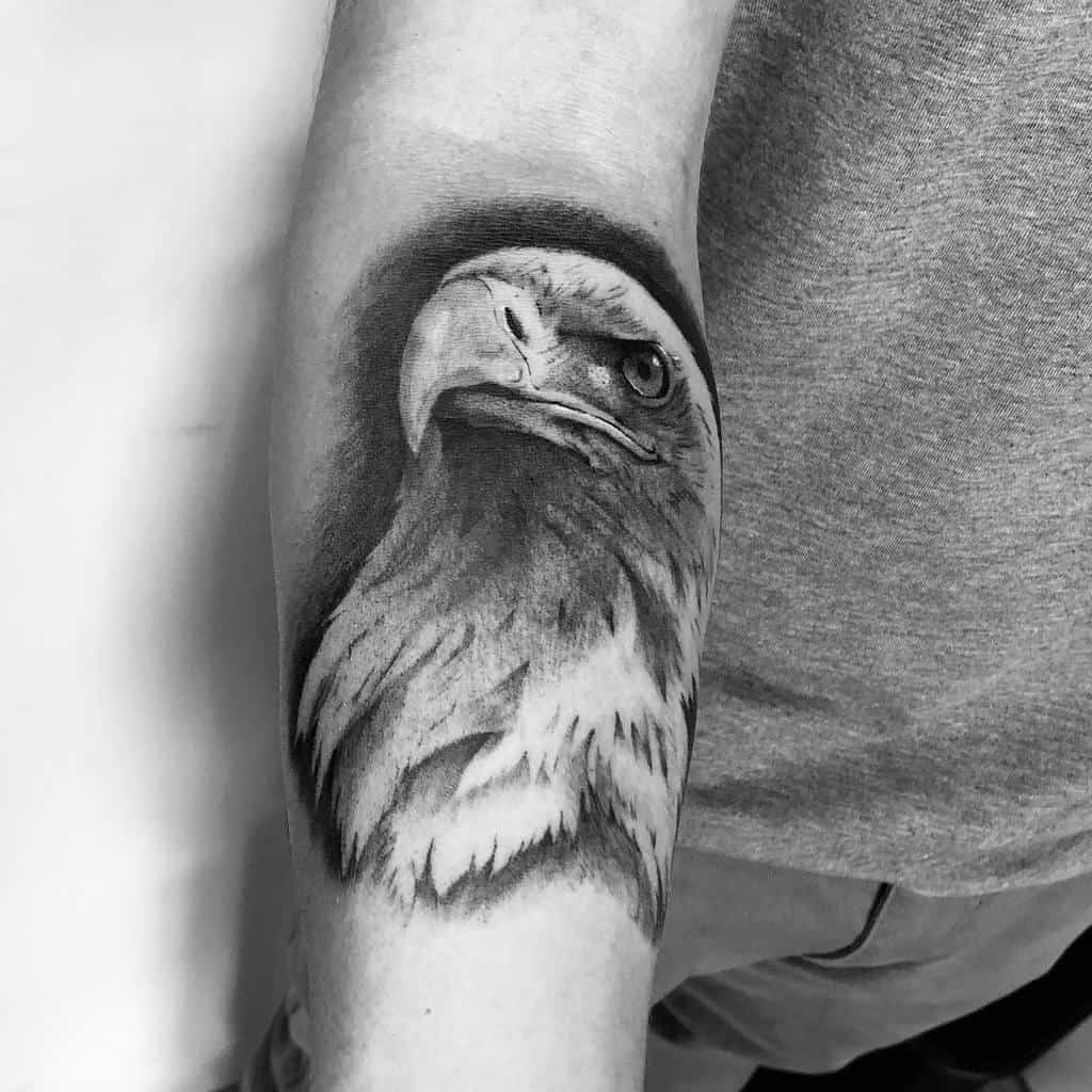 Black and gray tattoo of an eagle's head on an arm, showing detailed feathers and a piercing gaze