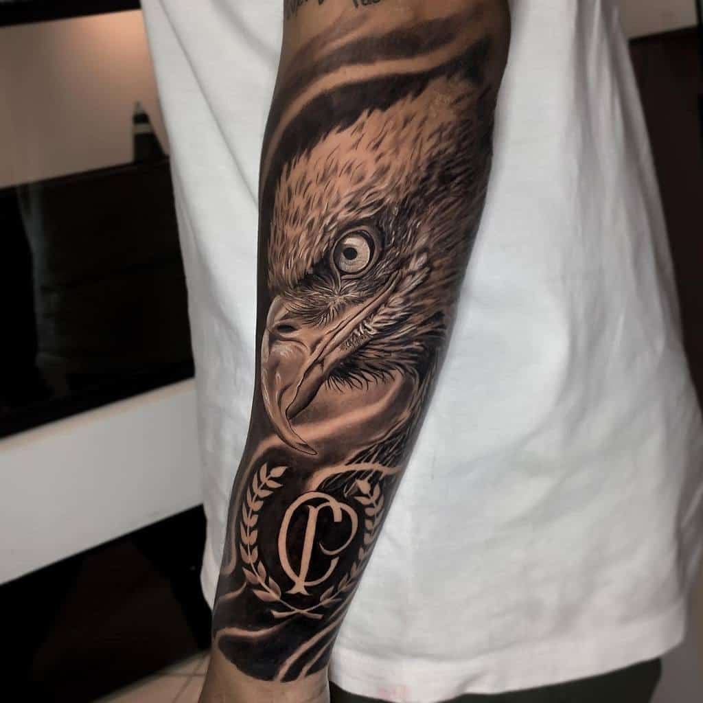 Forearm tattoo of a detailed eagle head with piercing eyes and a laurel wreath containing the lettera "CP"