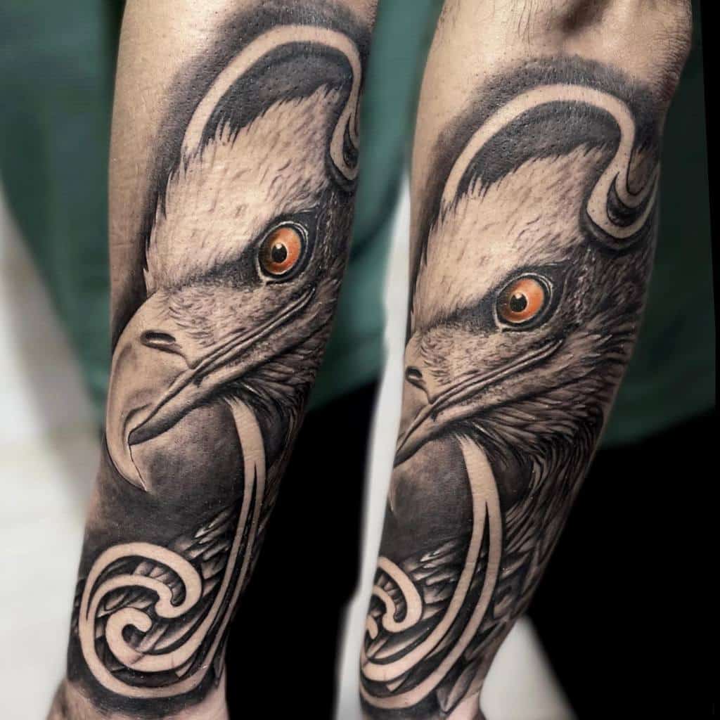 Close-up of a realistic tattoo of an eagle's head on two forearms featuring detailed feathers and piercing eyes