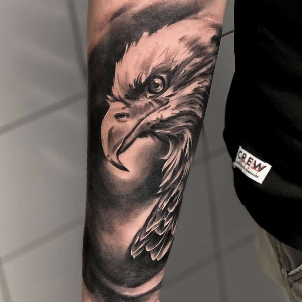A realistic tattoo of an eagle's head with intense eyes covers the forearm