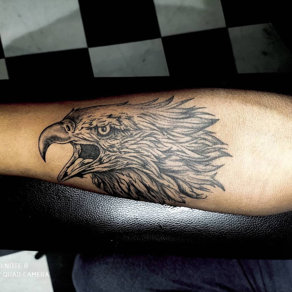 A detailed tattoo of an eagle's head in side profile is inked on a forearm