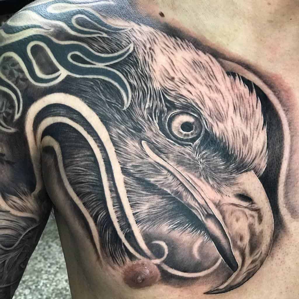 Tattoo of a detailed eagle's head on the upper chest and shoulder with flame-like elements around it