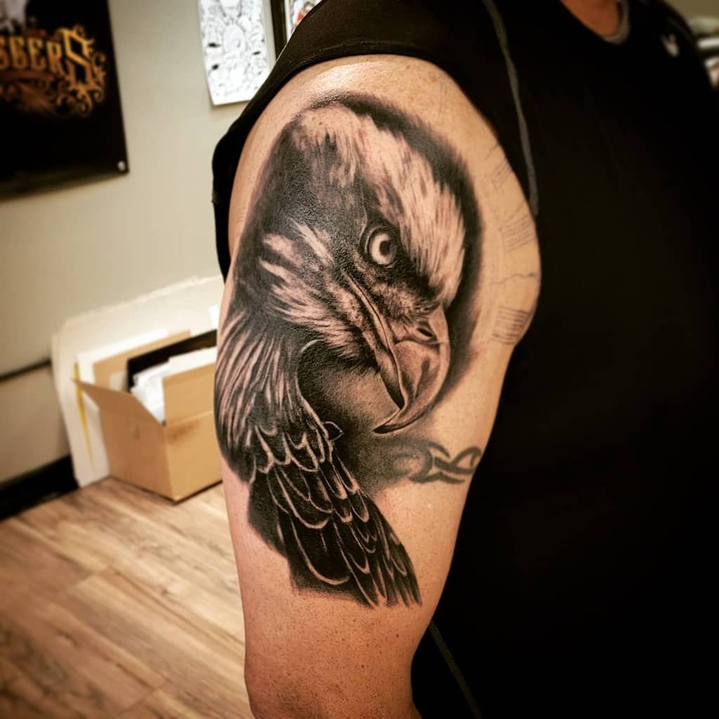 A detailed eagle head tattoo on a shoulder, showing the bird's intense gaze and feather details