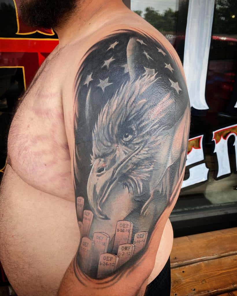 Detailed black and gray eagle htattoo on upper arm with American flag ead elements and dates