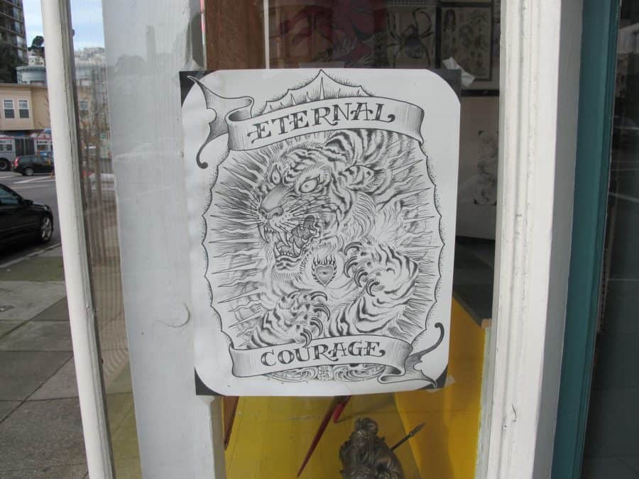 Tattoo-style illustration of a roaring tiger surrounded by flames, with the words "Eternal Courage" above and below it