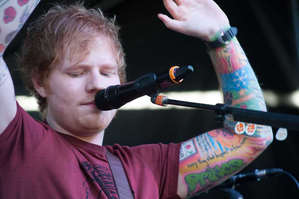 Ed Sheeran with colorful tattoos such as Heinz Ketchup, text of "Prince", text of "everything that happens is from home", ect.