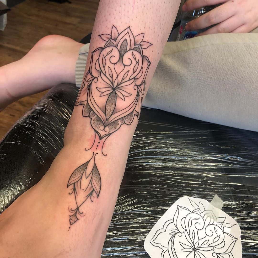 A forearm tattoo in progress, featuring an intricate lotus flower design with detailed line work and shading