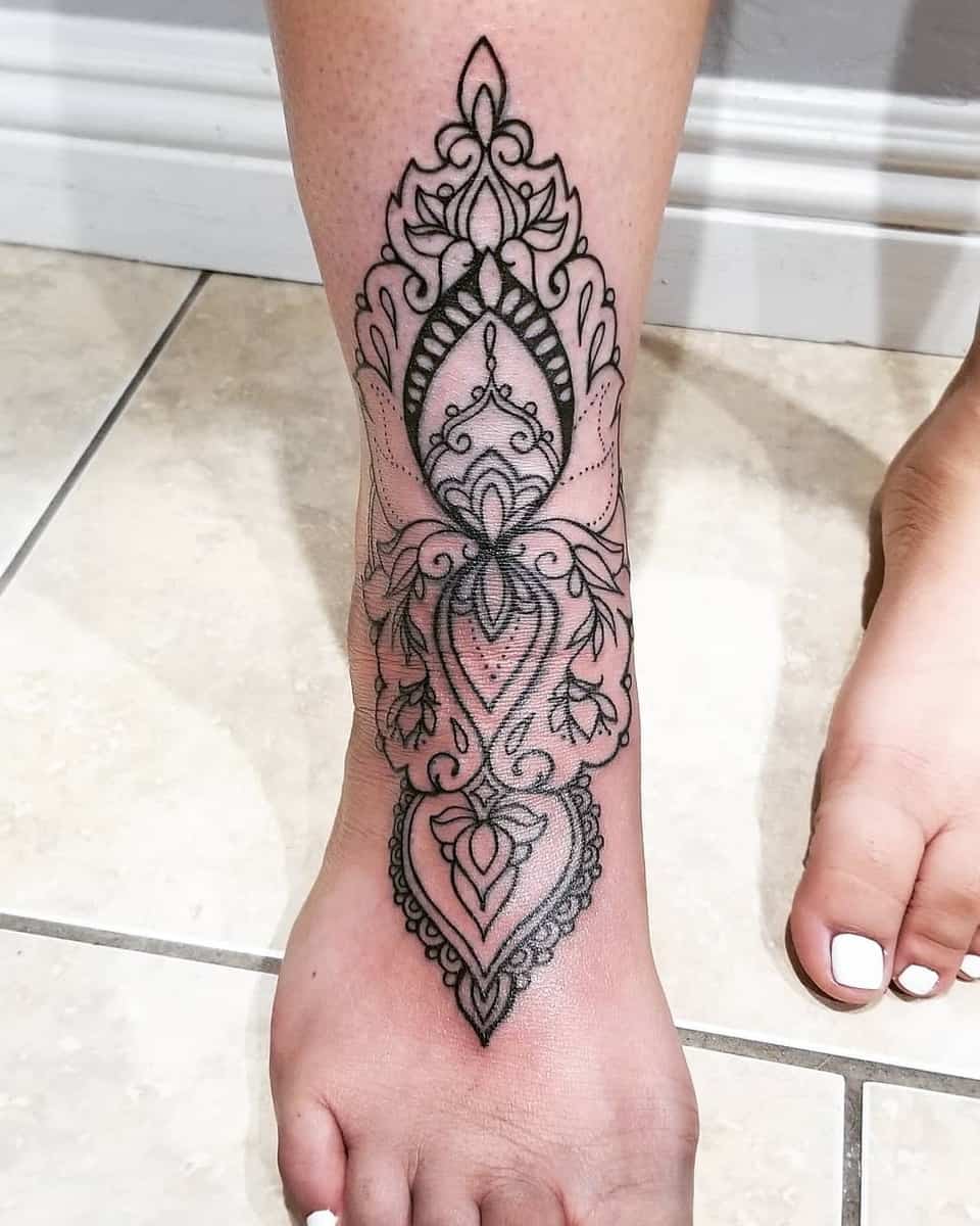 Ornate black ink tattoo with geometric and floral motifs on a lower leg and foot