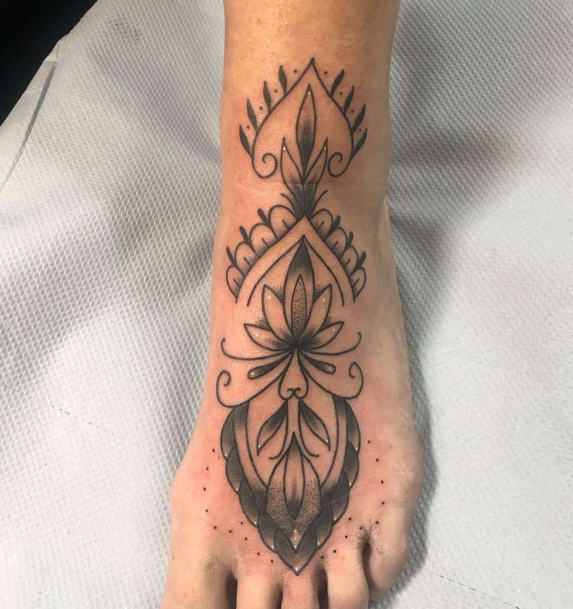 Intricate black ink floral and geometric tattoo design on the top of a foot