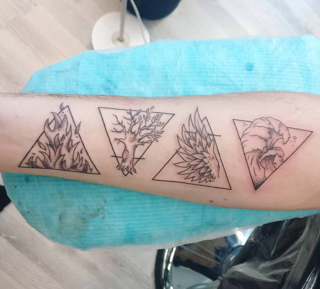 Forearm tattoo featuring designs of fire, tree, feathers, and an ocean wave