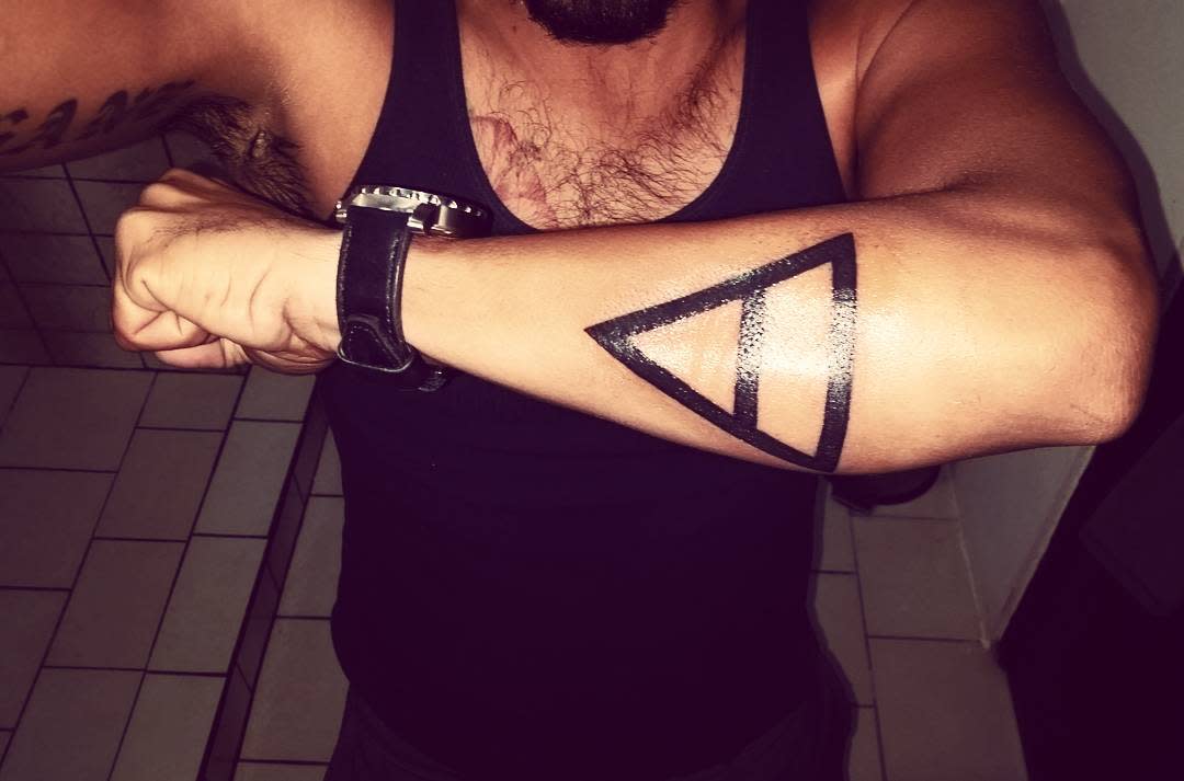 Arm tattoo of a solid black delta symbol - Earth symbol