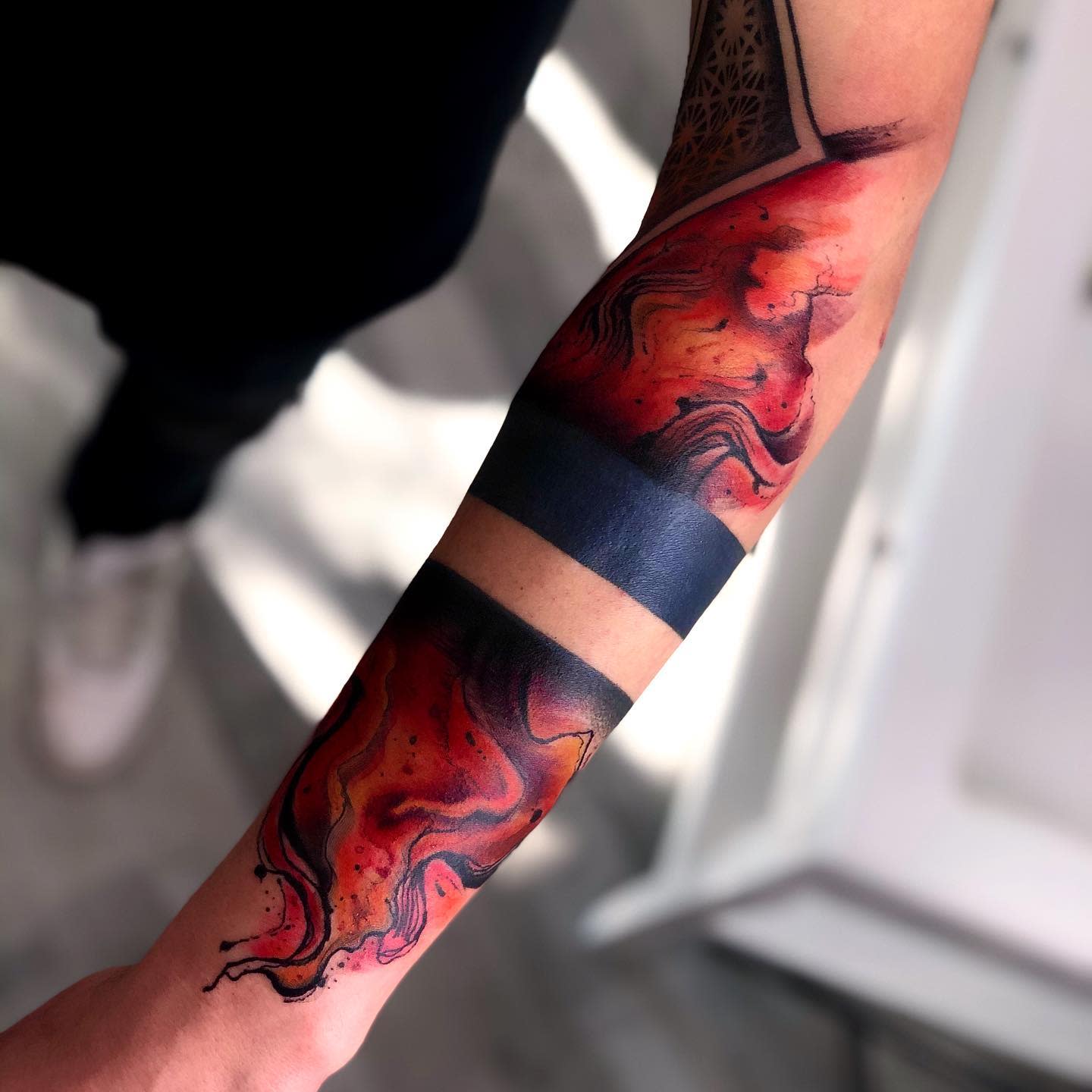A forearm tattoo with an abstract, fiery design and a solid black band