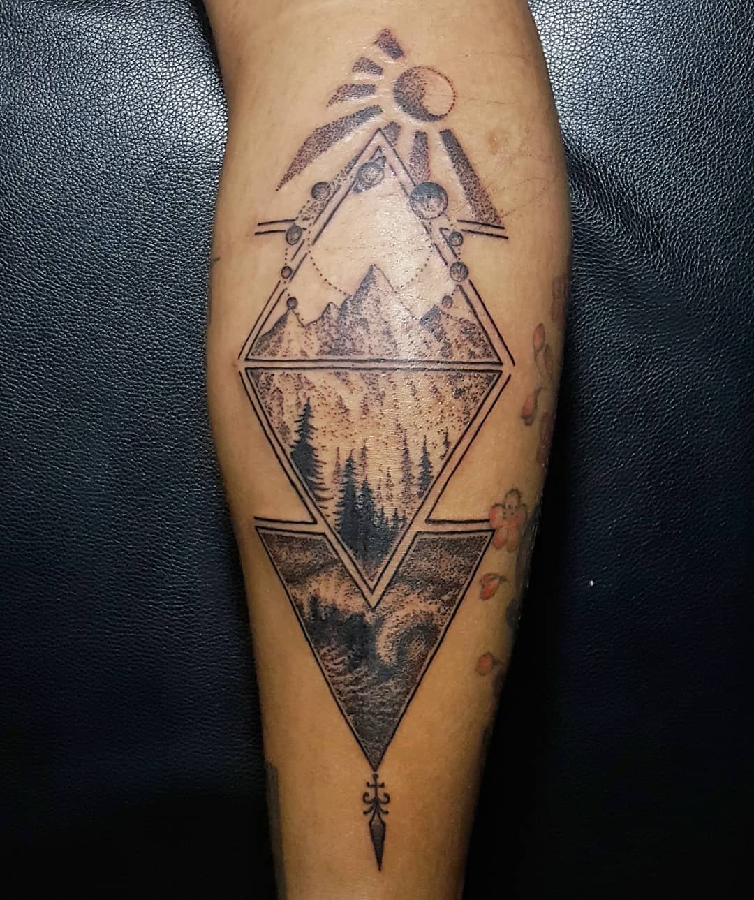 Geometric tattoo featuring mountains, forest, and celestial designs on an arm