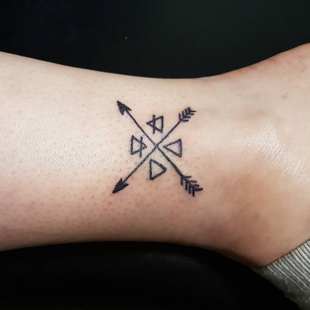 Tattoo of crossed arrows with geometric shapes on the side of an ankle