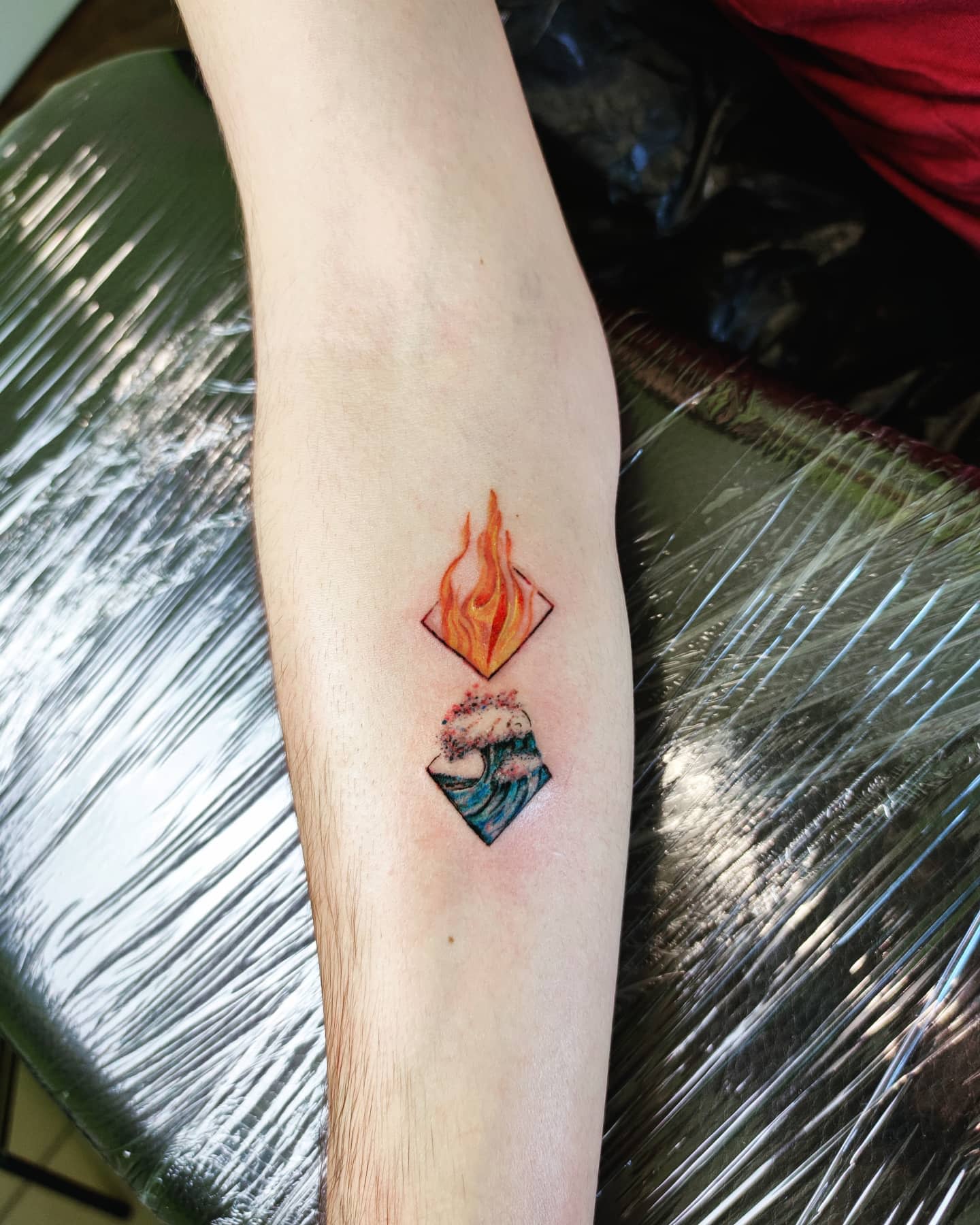 Tattoo of flames above waves inside diamond shapes on inner forearm