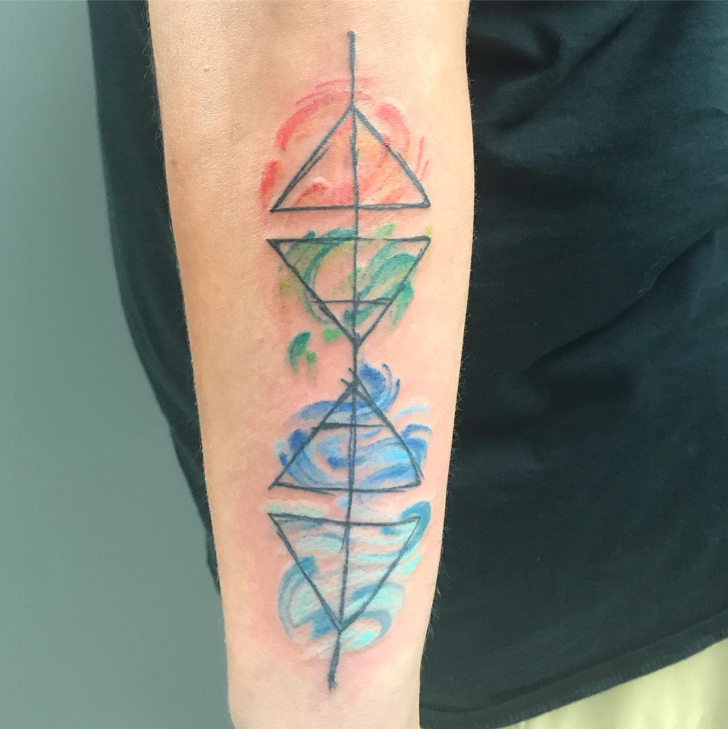 Forearm tattoo with three triangles and colorful watercolor splashes in red, green, and blue