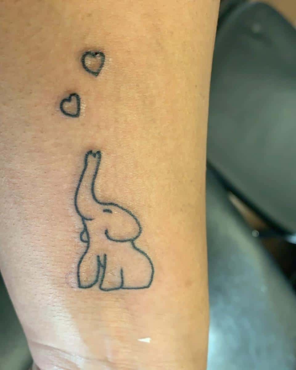 Outline tattoo of a small elephant with its trunk up, releasing three heart shapes above it
