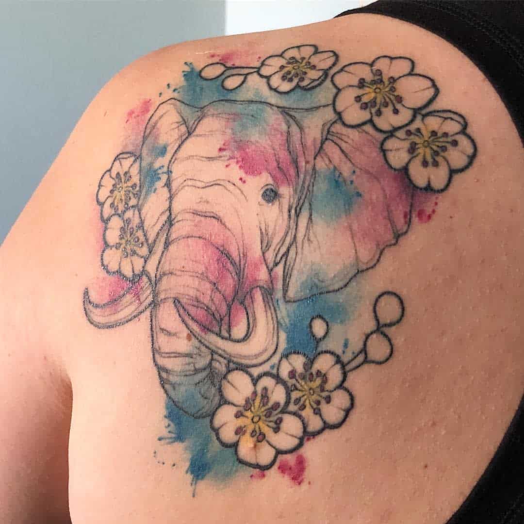 A watercolor-style tattoo of an elephant surrounded by flowers on a shoulder