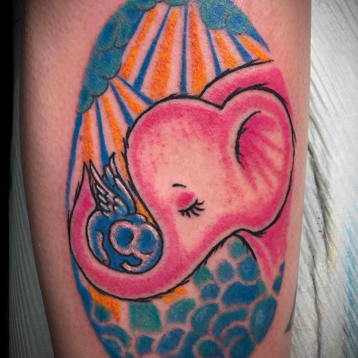 A colorful tattoo of a pink elephant cradling a small blue flying elephant with rays of orange in the background
