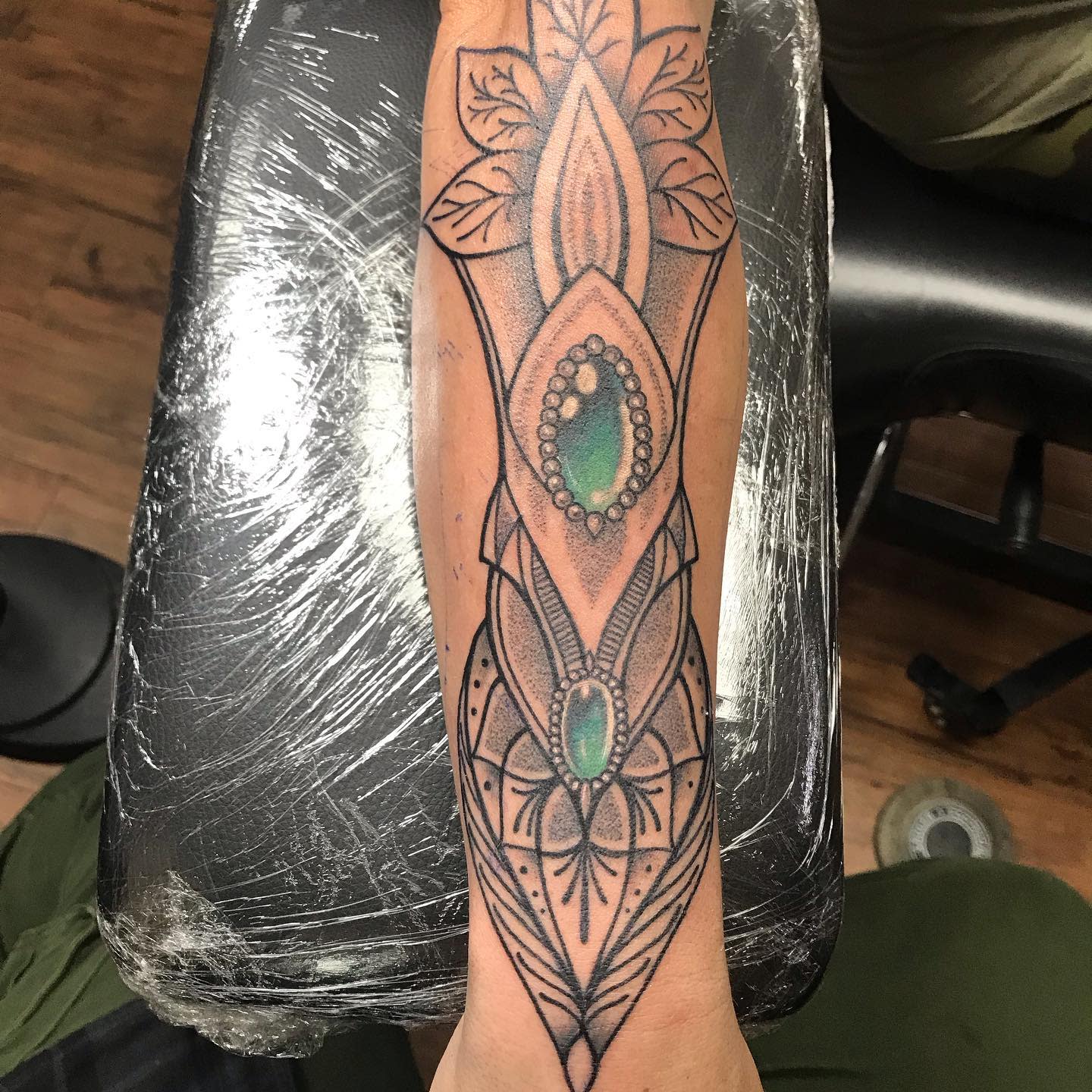 An ornate tattoo design with green gemstones on an inner forearm