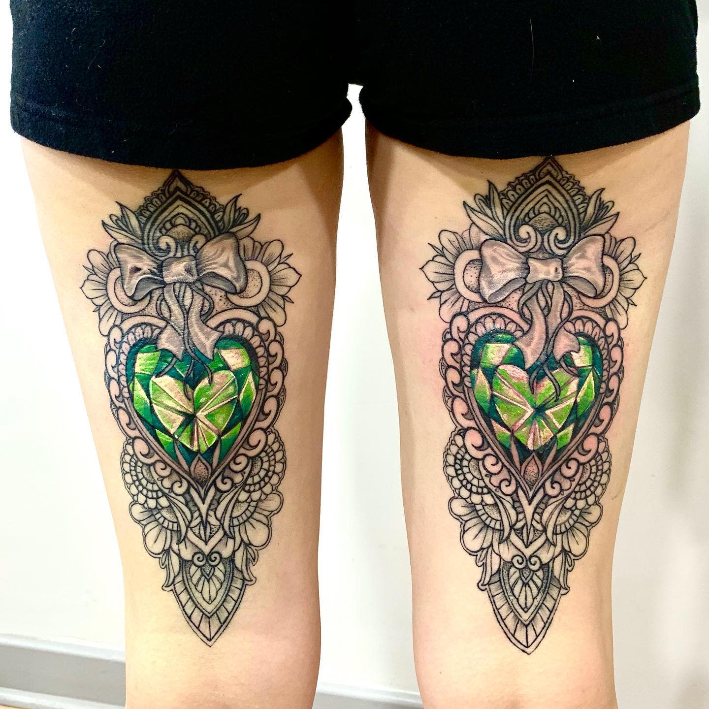 Matching ornamental tattoos of jeweled hearts with bows on the back of thighs
